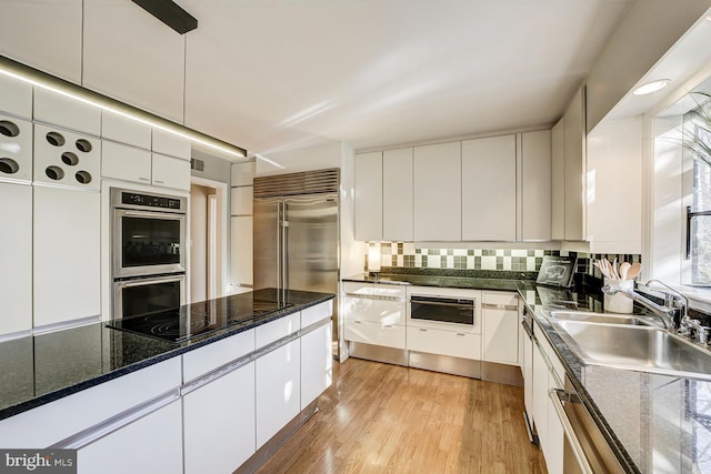 kitchen featuring white cabinets, decorative backsplash, appliances with stainless steel finishes, light wood-type flooring, and a sink