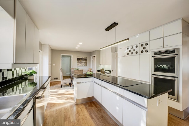 kitchen featuring stainless steel appliances, light wood finished floors, backsplash, and white cabinetry