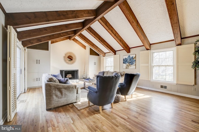 living area featuring baseboards, visible vents, lofted ceiling with beams, wood finished floors, and a fireplace