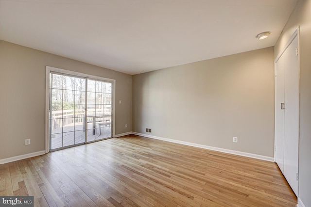 empty room with light wood finished floors, visible vents, and baseboards