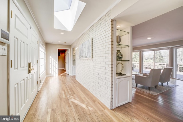 hallway with recessed lighting, brick wall, a skylight, light wood finished floors, and crown molding