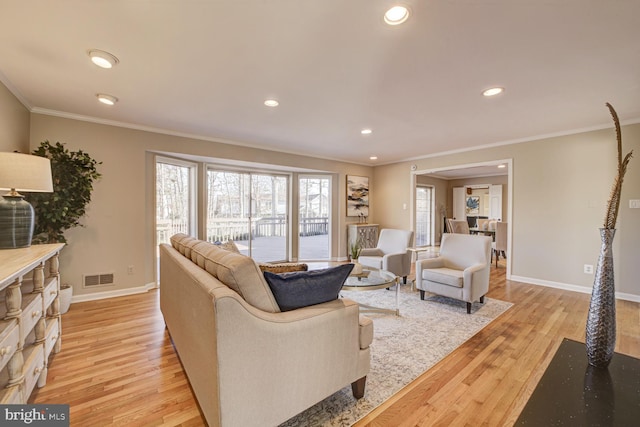 living room with ornamental molding, baseboards, visible vents, and light wood finished floors