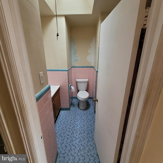 half bathroom featuring a wainscoted wall, tile walls, toilet, vanity, and tile patterned floors