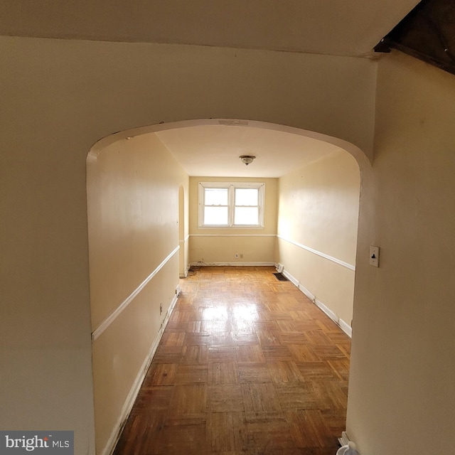 corridor featuring arched walkways and baseboards