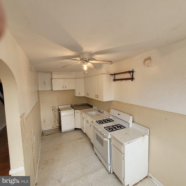 kitchen with a sink, white cabinets, wainscoting, white gas range oven, and light floors