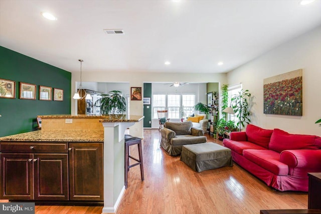 interior space featuring a breakfast bar area, light wood-style flooring, visible vents, open floor plan, and hanging light fixtures