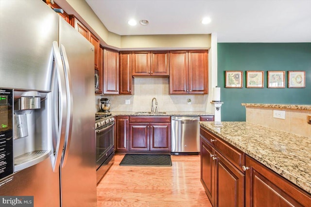 kitchen with appliances with stainless steel finishes, light wood-style floors, a sink, and light stone counters