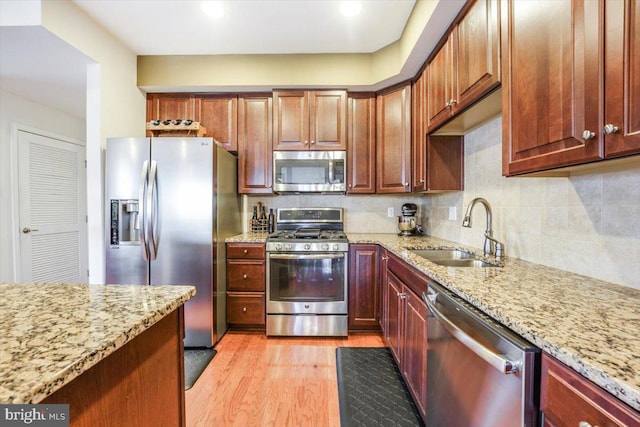 kitchen with decorative backsplash, light stone countertops, stainless steel appliances, light wood-style floors, and a sink