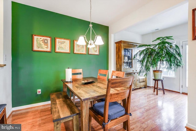 dining space featuring an accent wall, a notable chandelier, light wood-style flooring, and baseboards