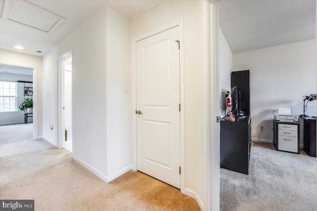 hall featuring light carpet, attic access, and baseboards