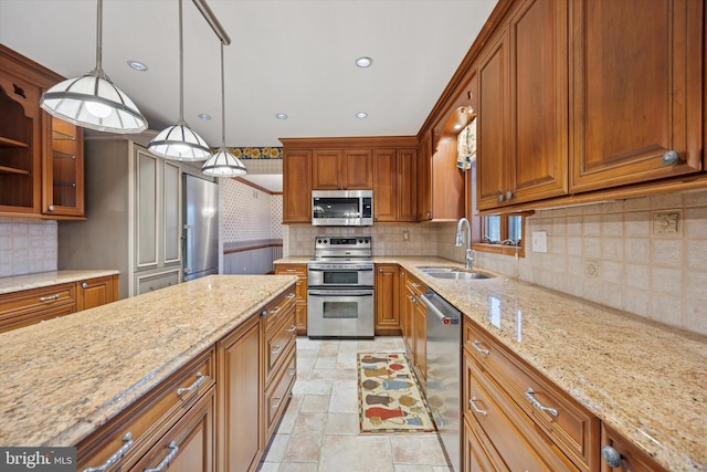 kitchen with appliances with stainless steel finishes, brown cabinetry, a sink, and light stone countertops