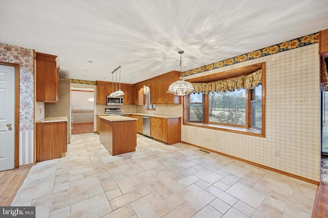 kitchen featuring appliances with stainless steel finishes, light countertops, a kitchen island, and wallpapered walls