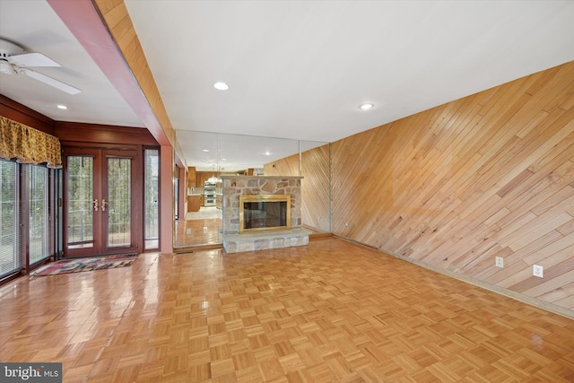 unfurnished living room featuring recessed lighting, wood walls, a stone fireplace, and ceiling fan