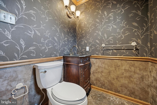 half bath featuring toilet, vanity, marble finish floor, wainscoting, and wallpapered walls