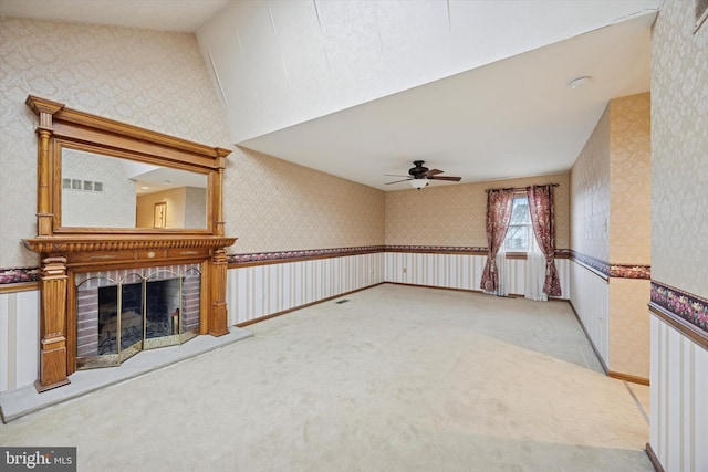 unfurnished living room with wallpapered walls, visible vents, vaulted ceiling, carpet flooring, and a fireplace