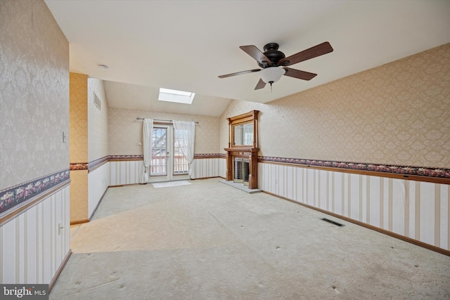 carpeted spare room featuring vaulted ceiling with skylight, a wainscoted wall, visible vents, and wallpapered walls