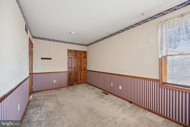 spare room featuring carpet floors, a wainscoted wall, and visible vents