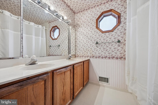 bathroom with double vanity, wallpapered walls, visible vents, and a sink