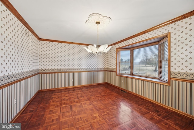 empty room with a notable chandelier, a wainscoted wall, visible vents, ornamental molding, and wallpapered walls