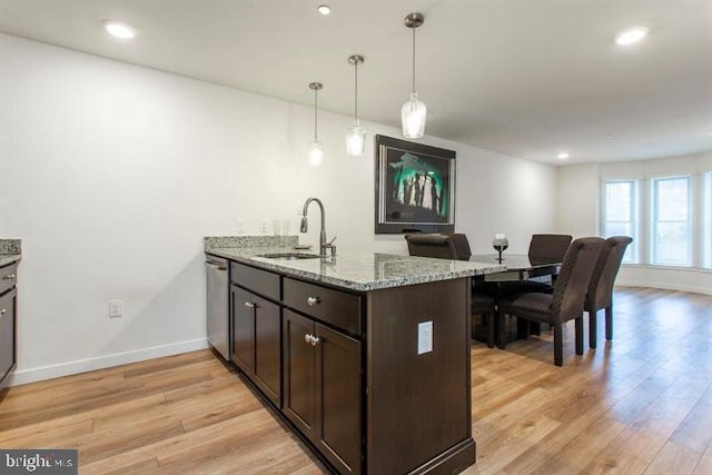 kitchen featuring dishwasher, light wood-style flooring, light stone counters, a peninsula, and a sink