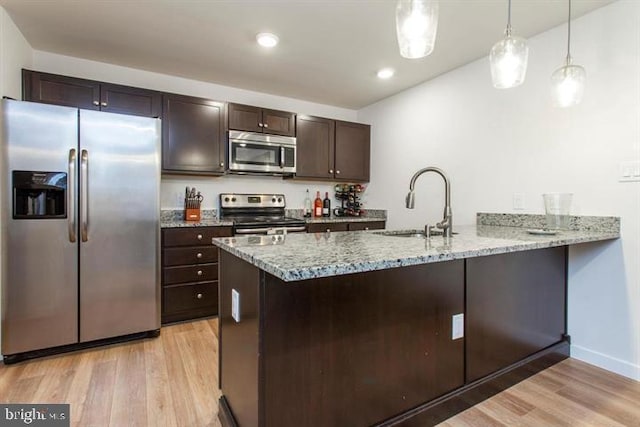 kitchen featuring pendant lighting, appliances with stainless steel finishes, a sink, light wood-type flooring, and a peninsula