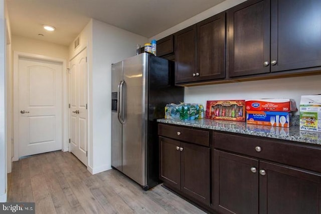 kitchen with light wood-style floors, dark stone counters, stainless steel refrigerator with ice dispenser, and dark brown cabinets