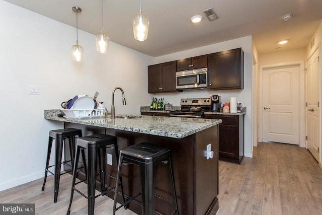 kitchen with appliances with stainless steel finishes, a sink, dark brown cabinetry, and pendant lighting