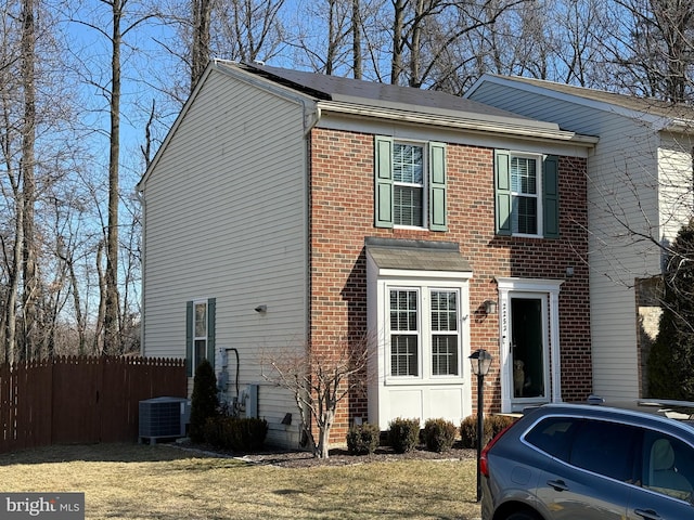 view of front facade featuring brick siding, a front lawn, central AC unit, and fence