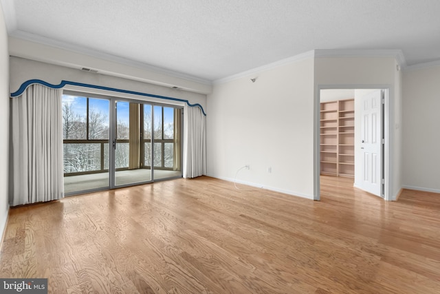 spare room with built in features, crown molding, light wood finished floors, a textured ceiling, and baseboards