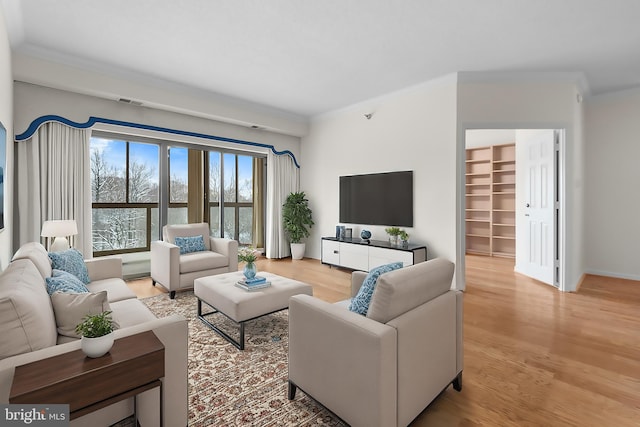 living area featuring ornamental molding, light wood finished floors, built in shelves, and baseboards