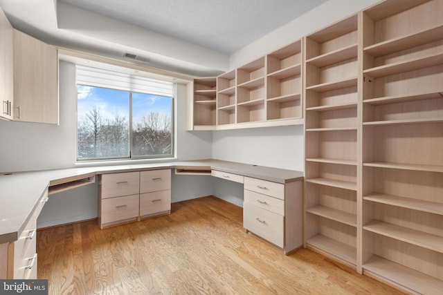 unfurnished office featuring light wood-style floors, a textured ceiling, visible vents, and built in desk