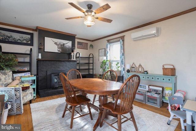 dining area featuring a wall unit AC, crown molding, a fireplace, and light hardwood / wood-style floors