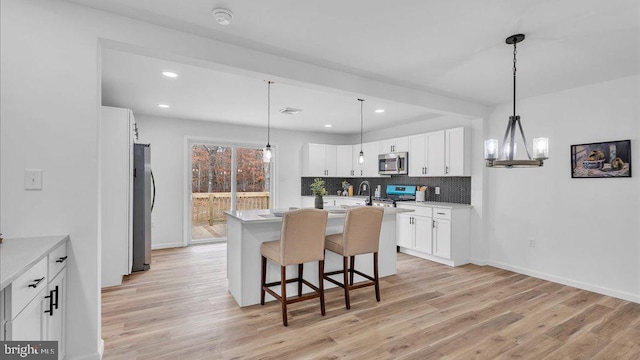 kitchen with a kitchen island with sink, stainless steel appliances, light wood-style floors, white cabinets, and decorative backsplash