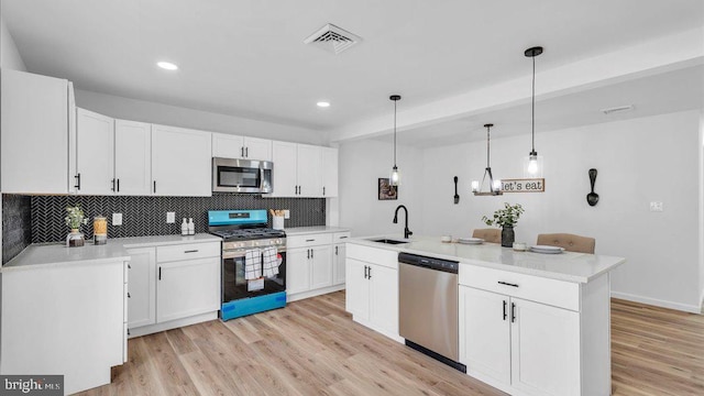 kitchen with white cabinets, stainless steel appliances, light countertops, pendant lighting, and a sink