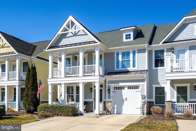 view of front of house with covered porch, concrete driveway, a standing seam roof, metal roof, and stone siding