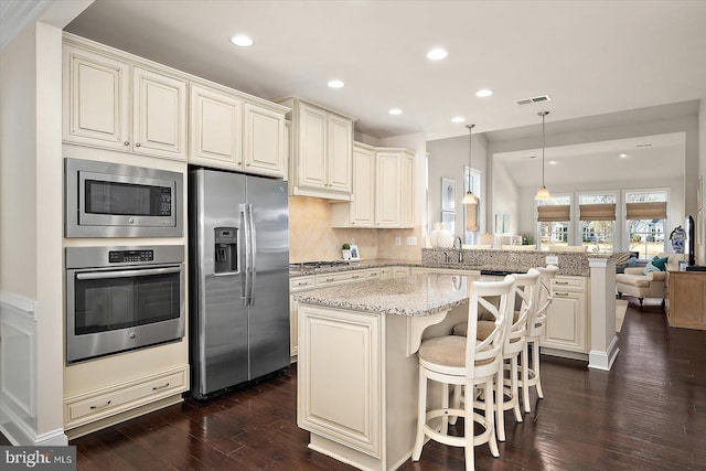 kitchen with a peninsula, a sink, a kitchen breakfast bar, appliances with stainless steel finishes, and dark wood finished floors