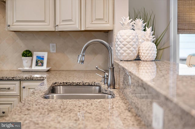 kitchen with light stone counters, cream cabinets, a sink, and decorative backsplash