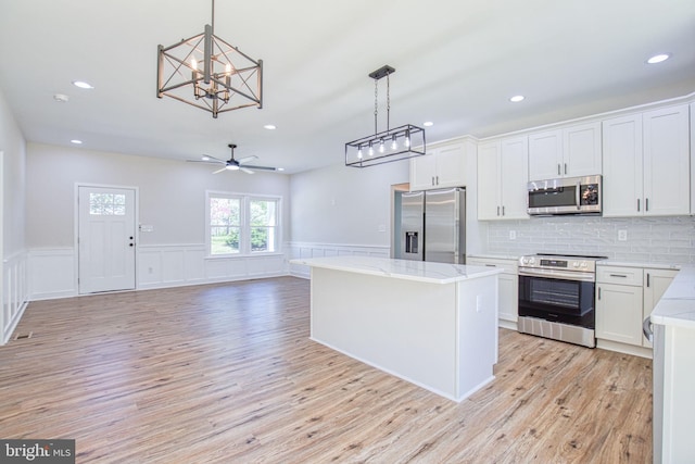 kitchen with light wood-style flooring, a kitchen island, white cabinets, appliances with stainless steel finishes, and hanging light fixtures