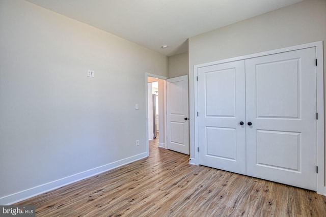 unfurnished bedroom featuring wood finished floors, baseboards, and a closet