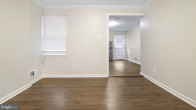 empty room with baseboards, visible vents, dark wood finished floors, and ornamental molding