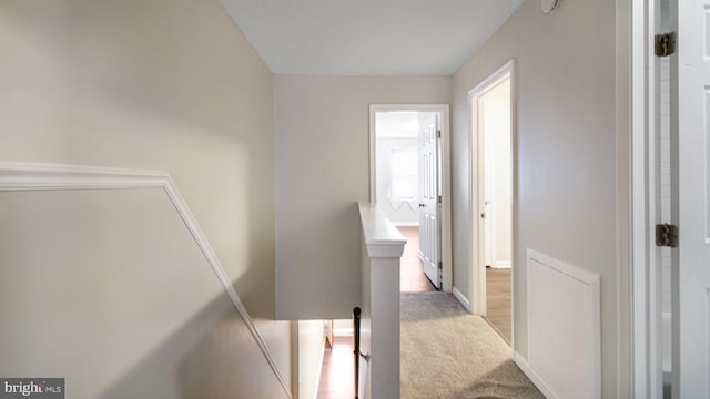 hallway featuring an upstairs landing, light carpet, and baseboards