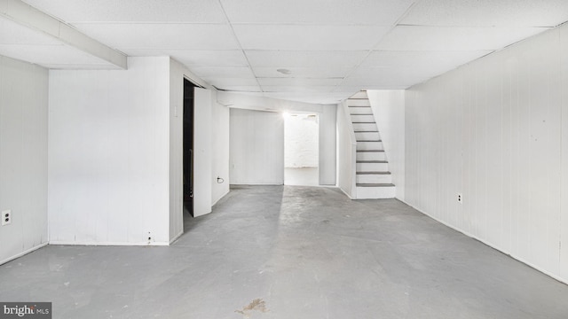 finished basement featuring a paneled ceiling, wood walls, and stairway