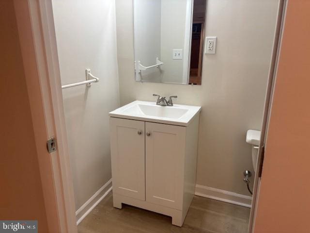 half bath with baseboards, wood finished floors, and vanity