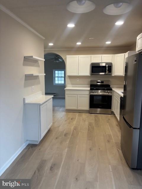 kitchen with arched walkways, stainless steel appliances, light wood-style floors, light countertops, and ornamental molding