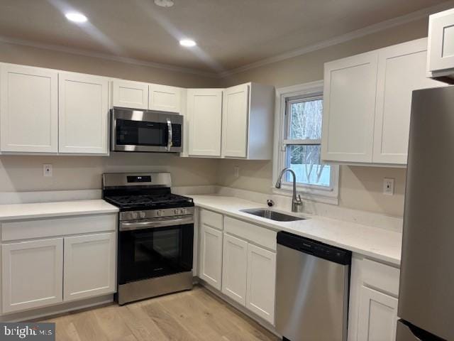 kitchen featuring appliances with stainless steel finishes, white cabinetry, a sink, and crown molding