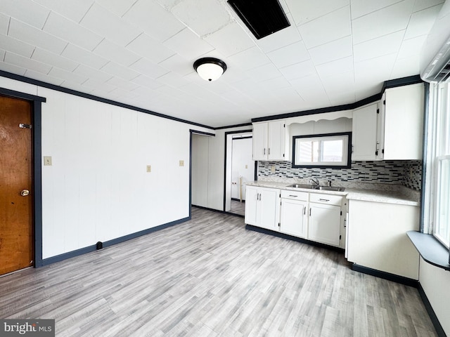 kitchen with light countertops, light wood-style flooring, decorative backsplash, white cabinetry, and a sink