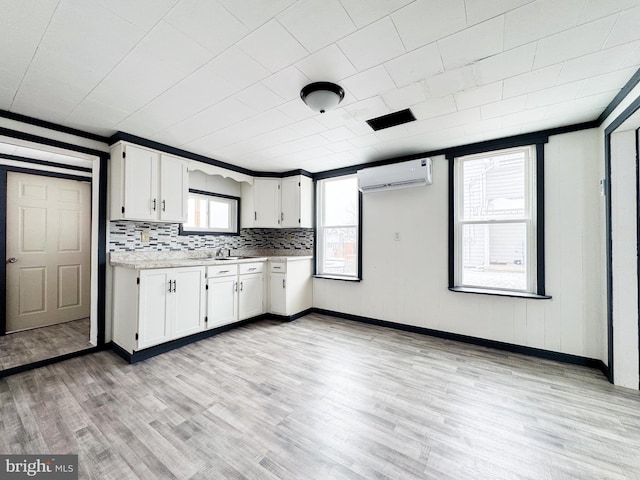 kitchen featuring light wood-type flooring, tasteful backsplash, white cabinets, and a wall mounted air conditioner