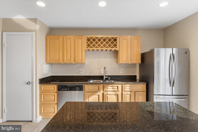 kitchen featuring dark stone countertops, stainless steel appliances, a sink, and light brown cabinetry