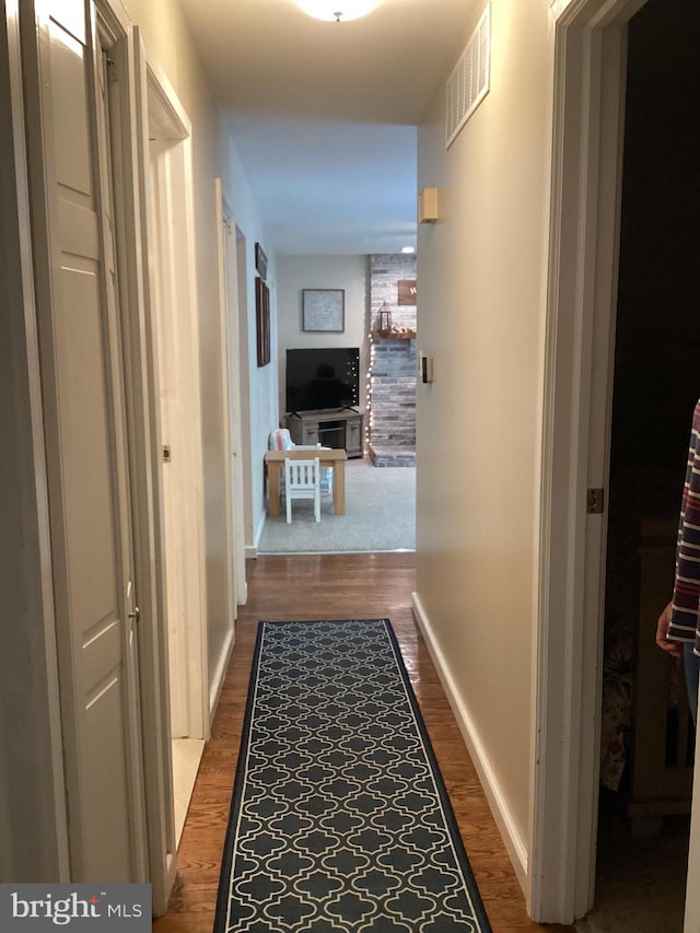 hall with baseboards, visible vents, and wood finished floors