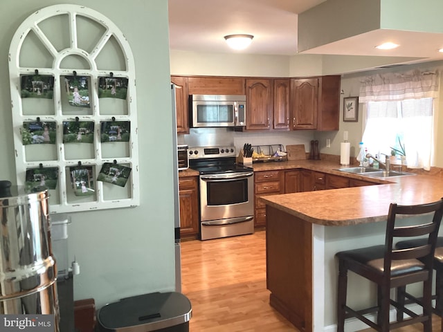 kitchen featuring a sink, a breakfast bar area, appliances with stainless steel finishes, light wood finished floors, and a peninsula